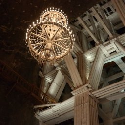 Foto Pablo Paweł Osiński - Wnętrze kopalni soli z drewnianą konstrukcją wsporczą i dwoma ozdobnymi żyrandolami z żarówkami, widok z dołu.