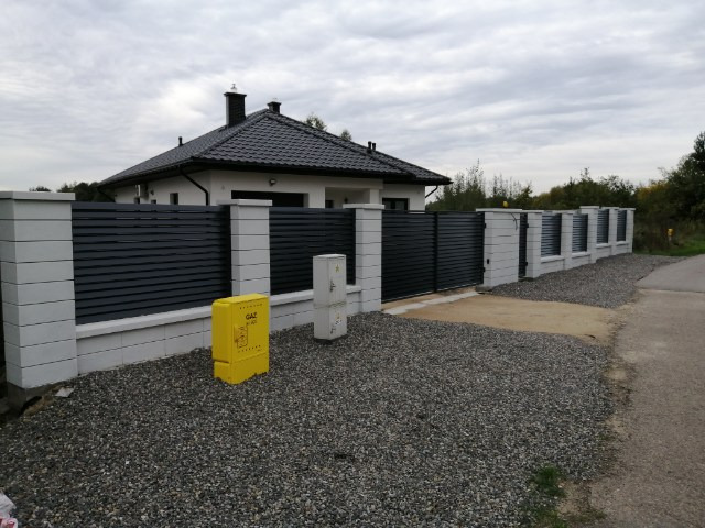 Nowoczesne ogrodzenie panelowe w kolorze antracytowym z betonowymi słupkami, widok z zewnątrz posesji, skrzynka gazowa na pierwszym planie.