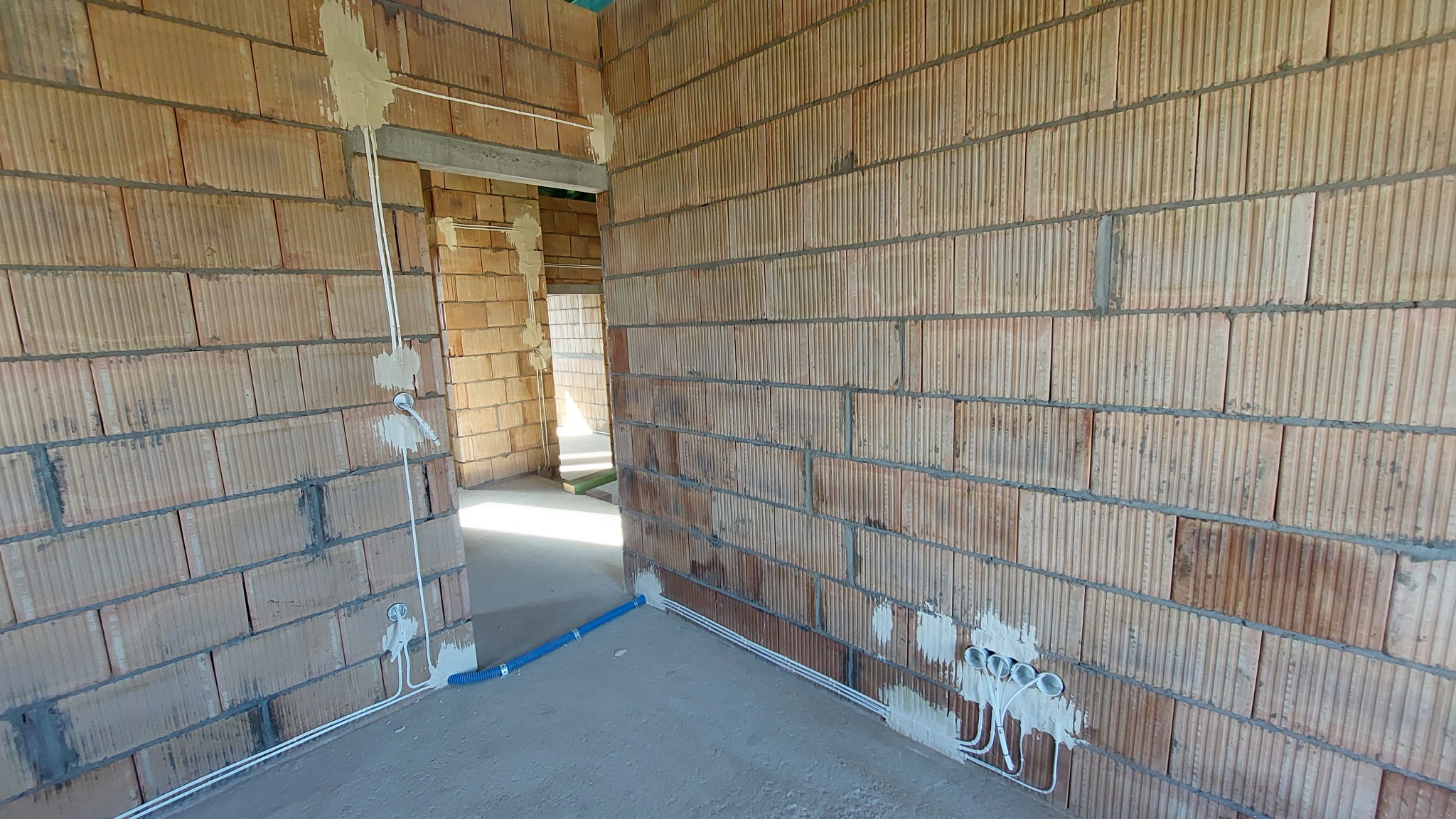 Wnętrze w trakcie prac wykończeniowych, widoczne ściany z cegły dziurawki z poprowadzonymi przewodami elektrycznymi w peszlach i puszkami podtynkowymi, oraz fragment instalacji wodnej...