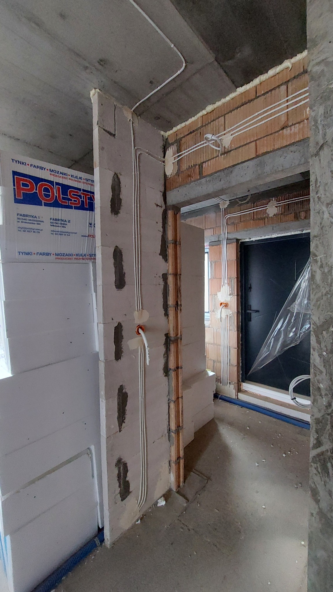 Wnętrze w trakcie prac wykończeniowych, widoczne przewody elektryczne prowadzone po ścianach z betonu komórkowego i cegły, zabezpieczone pianką montażową, z puszkami instalacyjnymi, na ścianie...