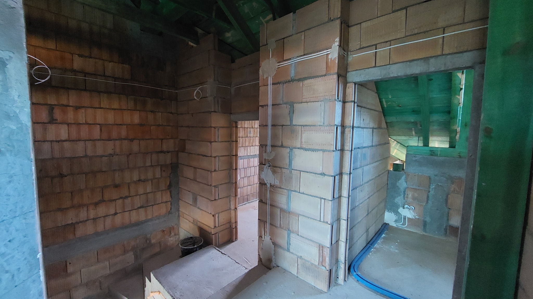 Wnętrze budynku w trakcie budowy z widocznymi instalacjami kabli elektrycznych prowadzonymi po ścianach z cegły ceramicznej.