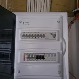 Otwarta skrzynka elektryczna z bezpiecznikami EATON i przewodami u góry oraz po bokach, zamontowana na szorstkiej ścianie.