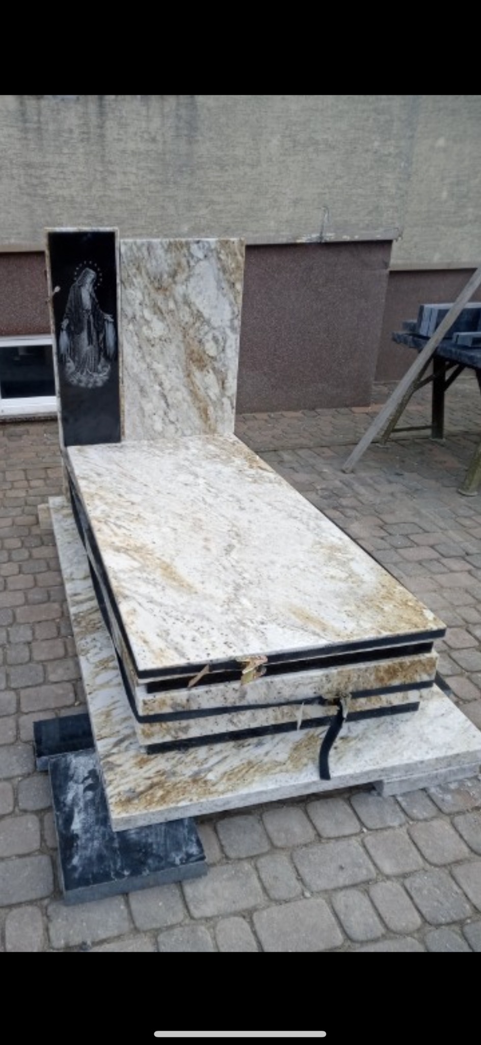 Elementy granitowe z wygrawerowanym wizerunkiem Matki Boskiej, przygotowane do montażu, z widocznymi czarnymi przekładkami między płytami.