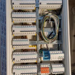 Rozdzielnica elektryczna z zainstalowanymi bezpiecznikami, przewodami i innymi elementami, widoczne kable w różnych kolorach, listwy zaciskowe i zabezpieczenia przepięciowe, widok z bliska.