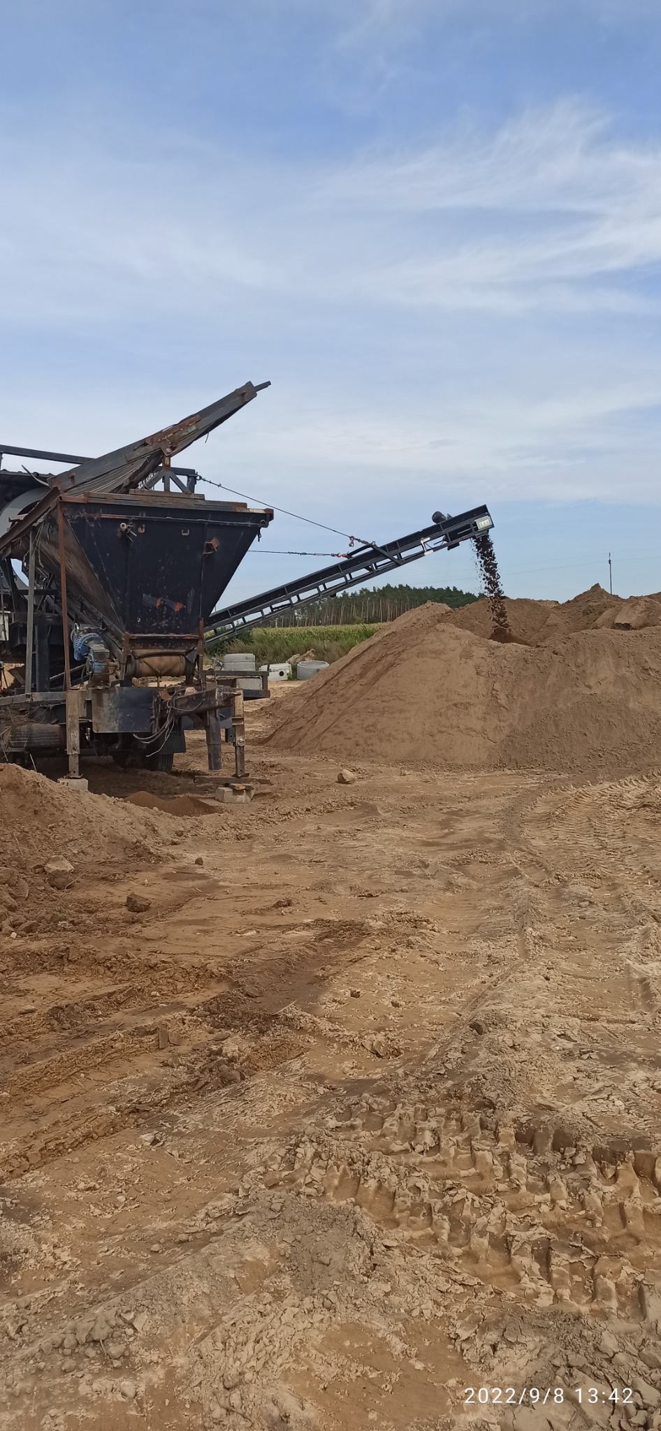 Praca przesiewacza mobilnego na placu budowy; przesypywanie materiału z taśmociągu na pryzmę.