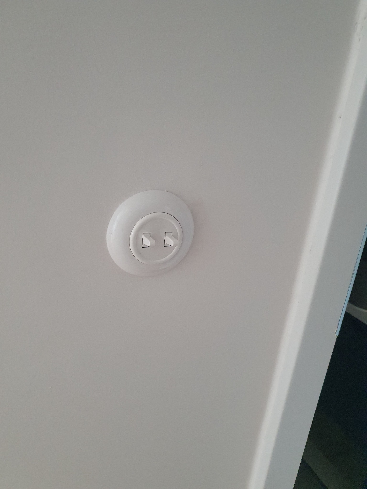Białe gniazdko elektryczne natynkowe z dwoma włącznikami, zamontowane na białej ścianie, widoczne pod kątem.