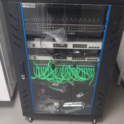 Maciej Wegiera ELEKTRONIK - Szafa rackowa z zainstalowanymi przełącznikami sieciowymi i patch panelem, okablowanie w kolorze zielonym, widoczne elementy montażowe wewnątrz szafy.