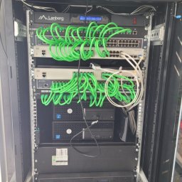 Maciej Wegiera ELEKTRONIK - Szafa rackowa z zamontowanymi urządzeniami sieciowymi: switche, routery, serwery i zasilacz awaryjny, połączone zielonymi kablami patchcord, widoczne oznaczenia Lanberg i Planet.