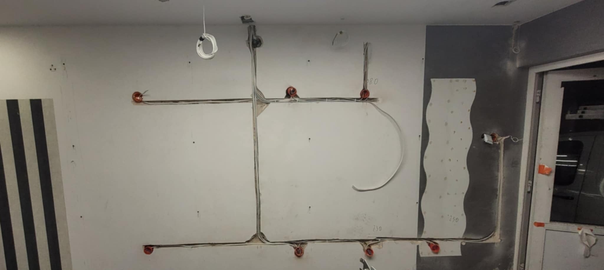 Elektryczne przewody rozprowadzone po ścianie w trakcie remontu w Łodzi, widoczne puszki instalacyjne i fragmenty kabli zwisających z sufitu.