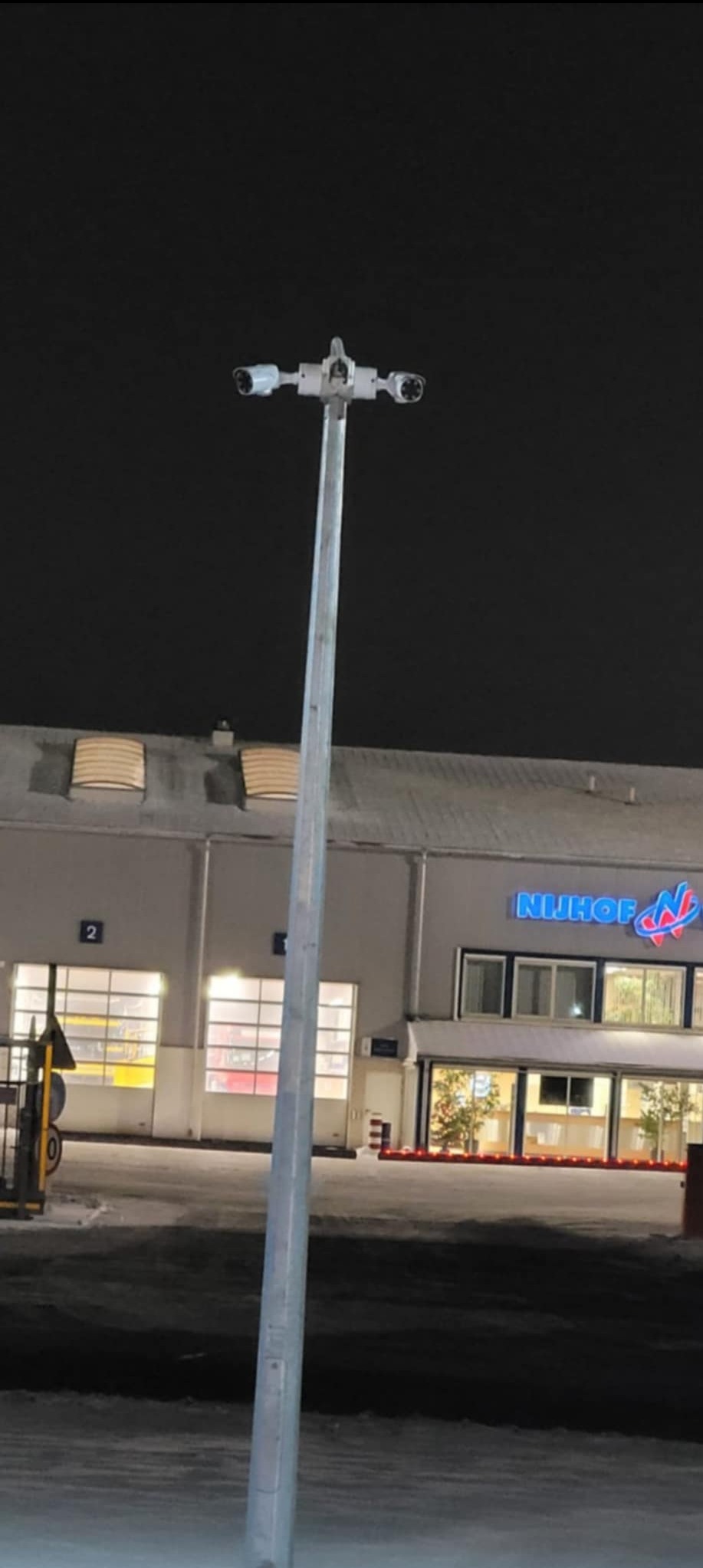 Słup z czterema kamerami przemysłowymi na zewnątrz budynku firmy Nijhof w nocy.
