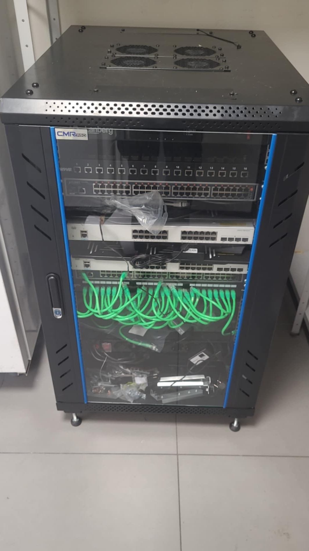 Szafa rackowa z zainstalowanymi przełącznikami sieciowymi i patch panelem, okablowanie w kolorze zielonym, widoczne elementy montażowe wewnątrz szafy.