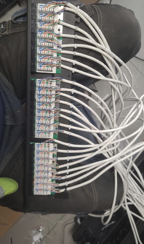 Panel krosowniczy z podłączonymi kablami sieciowymi, widok z góry, fragment stroju roboczego w kadrze.