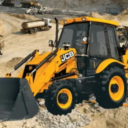 Żółto-czarna koparko-ładowarka JCB na placu budowy z piaskiem i innymi ciężarówkami w tle.