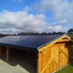 Nowoczesna wiata garażowa z drewnianą konstrukcją i panelami fotowoltaicznymi na dachu, na tle błękitnego nieba z chmurami.