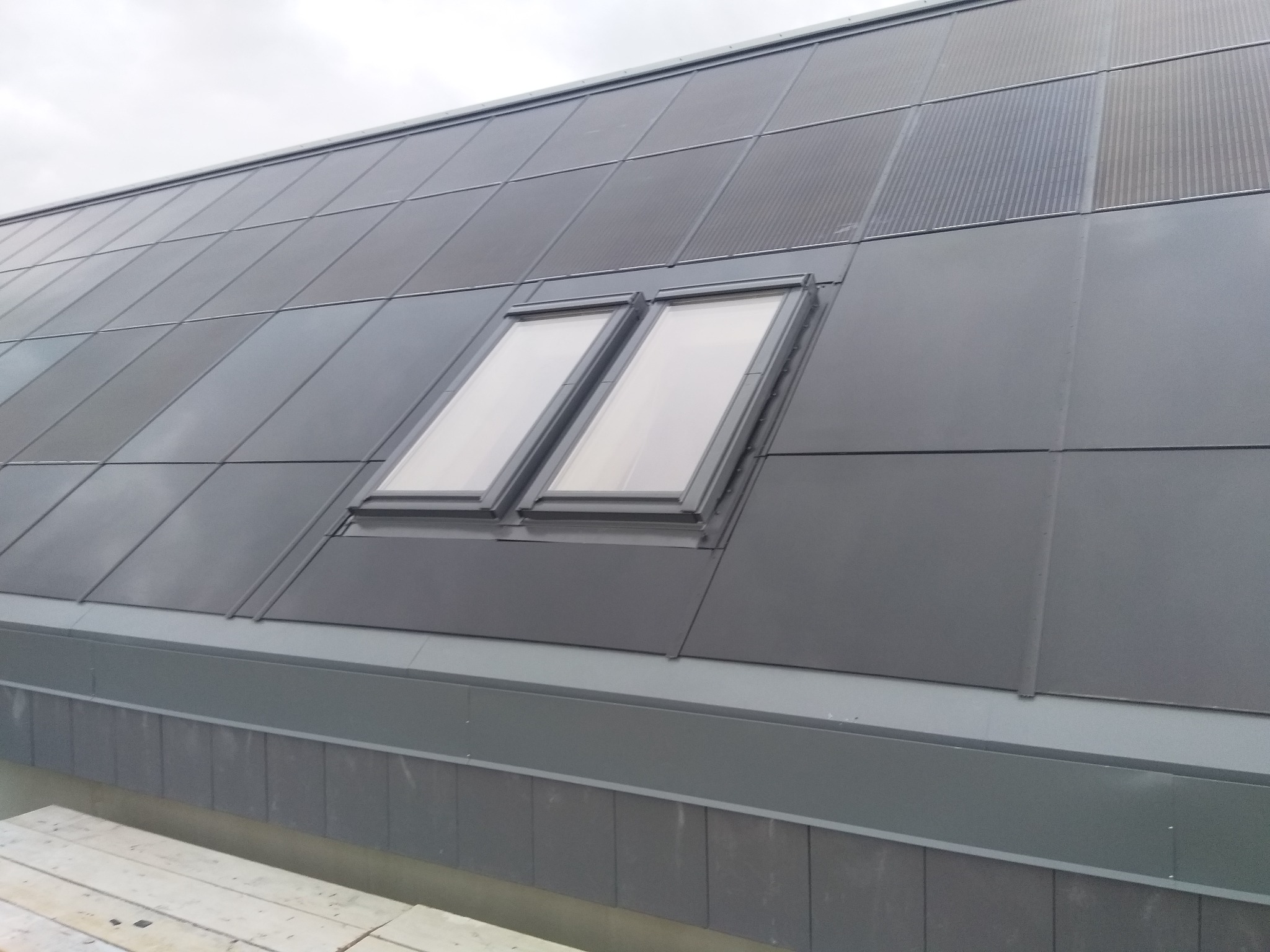 Szary dach z blachy na rąbek stojący z dwoma oknami dachowymi, widok z dołu.