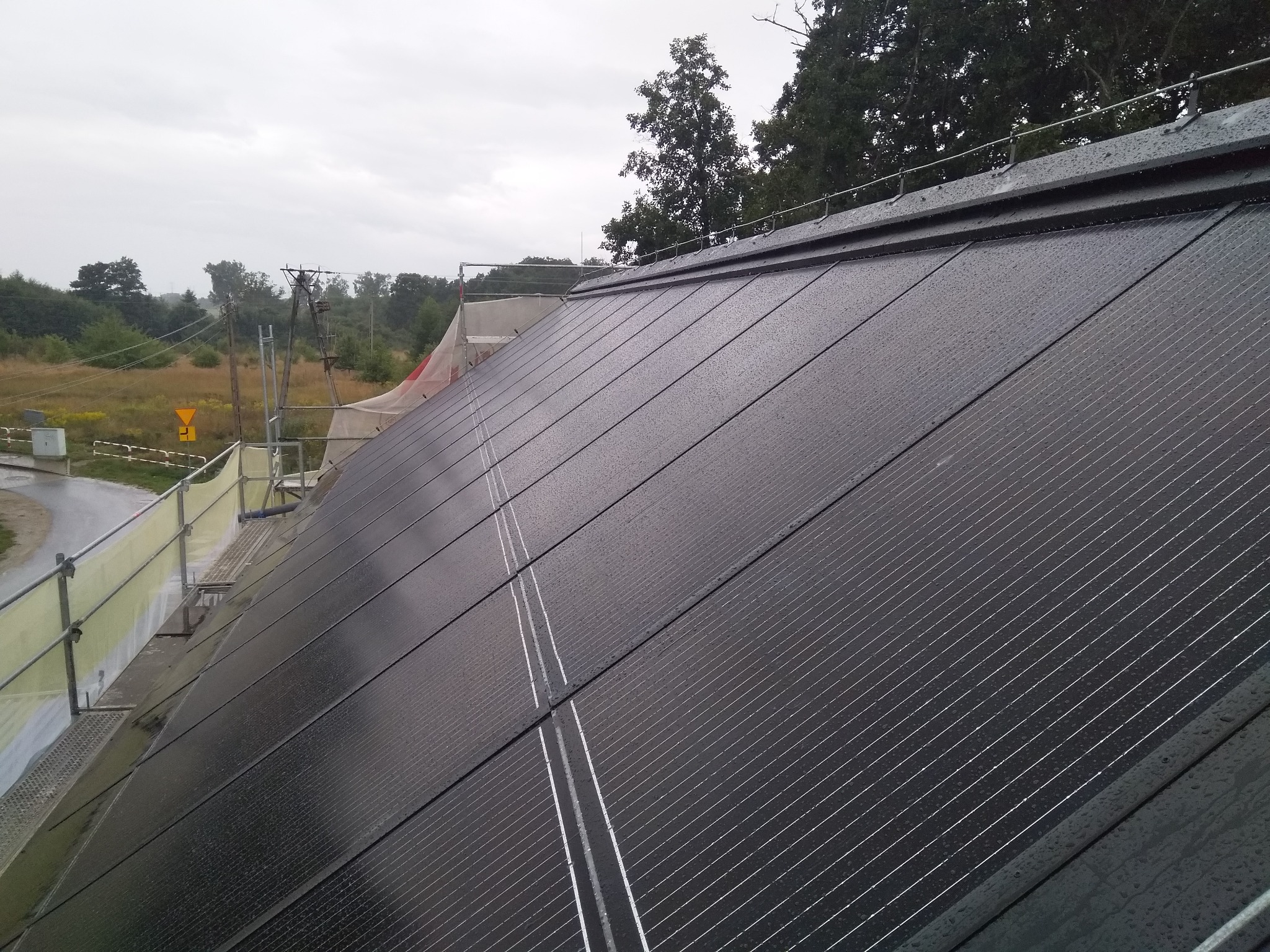 Montaż paneli fotowoltaicznych na dachu budynku we Wrocławiu, widoczne rusztowanie i krople deszczu na panelach.