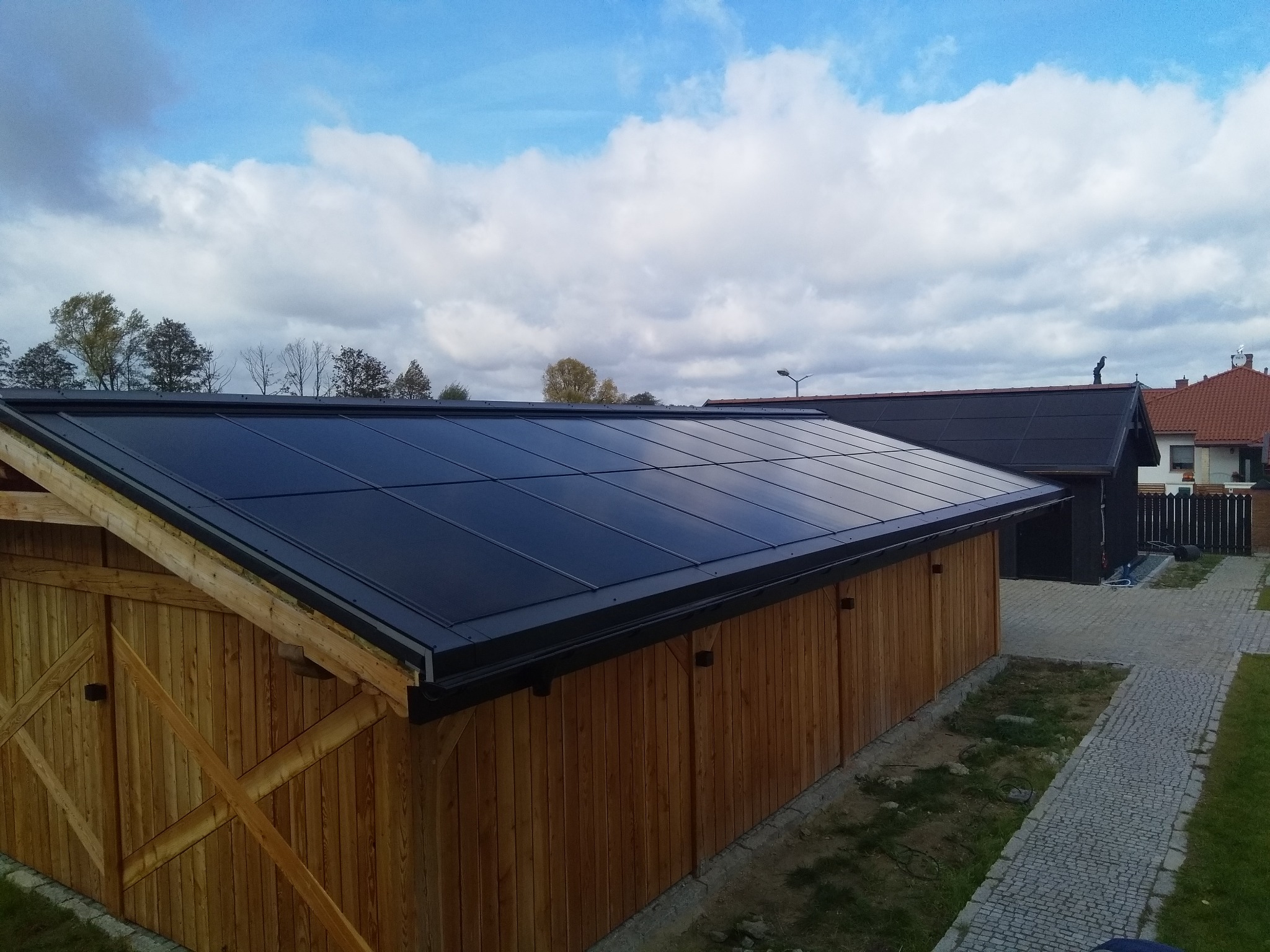 Nowoczesny, płaski dach z paneli na drewnianej konstrukcji, widok z góry na tle błękitnego nieba z chmurami.