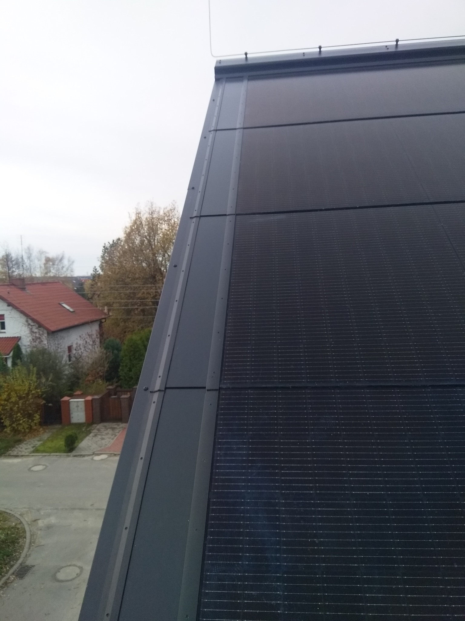 Nowoczesny dach z paneli fotowoltaicznych, widok z góry, z widocznym fragmentem ulicy i domu w tle.