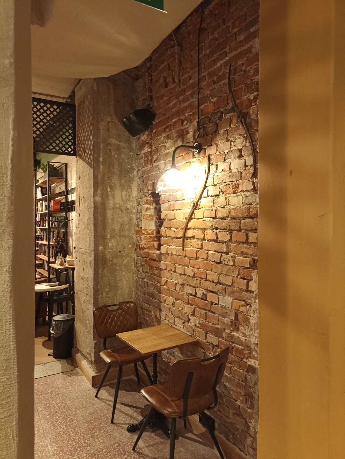 Kącik kawiarniany z ceglaną ścianą, oświetleniem punktowym i stolikiem z dwoma krzesłami w klimatycznym wnętrzu.