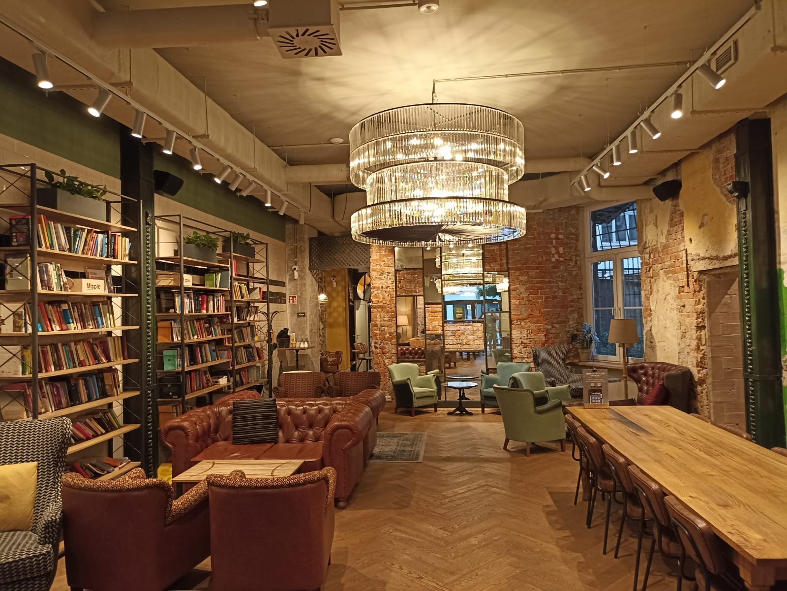 Wnętrze kawiarni z regałami pełnymi książek, skórzanymi sofami, drewnianym parkietem i ozdobnymi żyrandolami, oświetlone reflektorami punktowymi