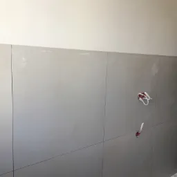 Ściana z zamontowanymi płytami gipsowo-kartonowymi, widoczne kable elektryczne wystające ze ściany i zaznaczone linie cięcia, w tle odkurzacz przemysłowy.