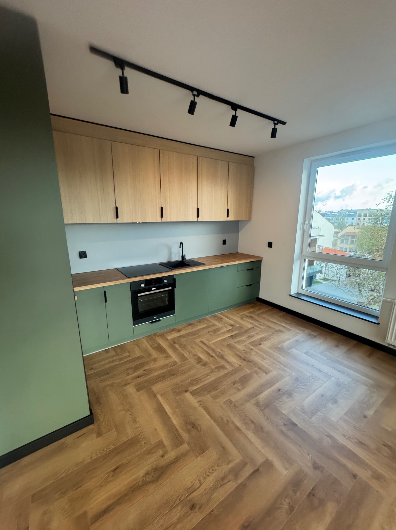 Nowoczesna kuchnia we Wrocławiu z zielonymi szafkami i drewnianym blatem. Uwagę przykuwa parkiet ułożony w jodełkę oraz listwa z reflektorami.