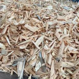 Jasne zrębki drzewne o nieregularnych kształtach, wypełniające przestrzeń z widocznym ciemnym tłem u góry.