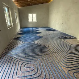 Niebieskie rury ogrzewania podłogowego na folii z siatką w surowym wnętrzu. Montaż instalacji w Cieszanowie przed wylaniem posadzki.