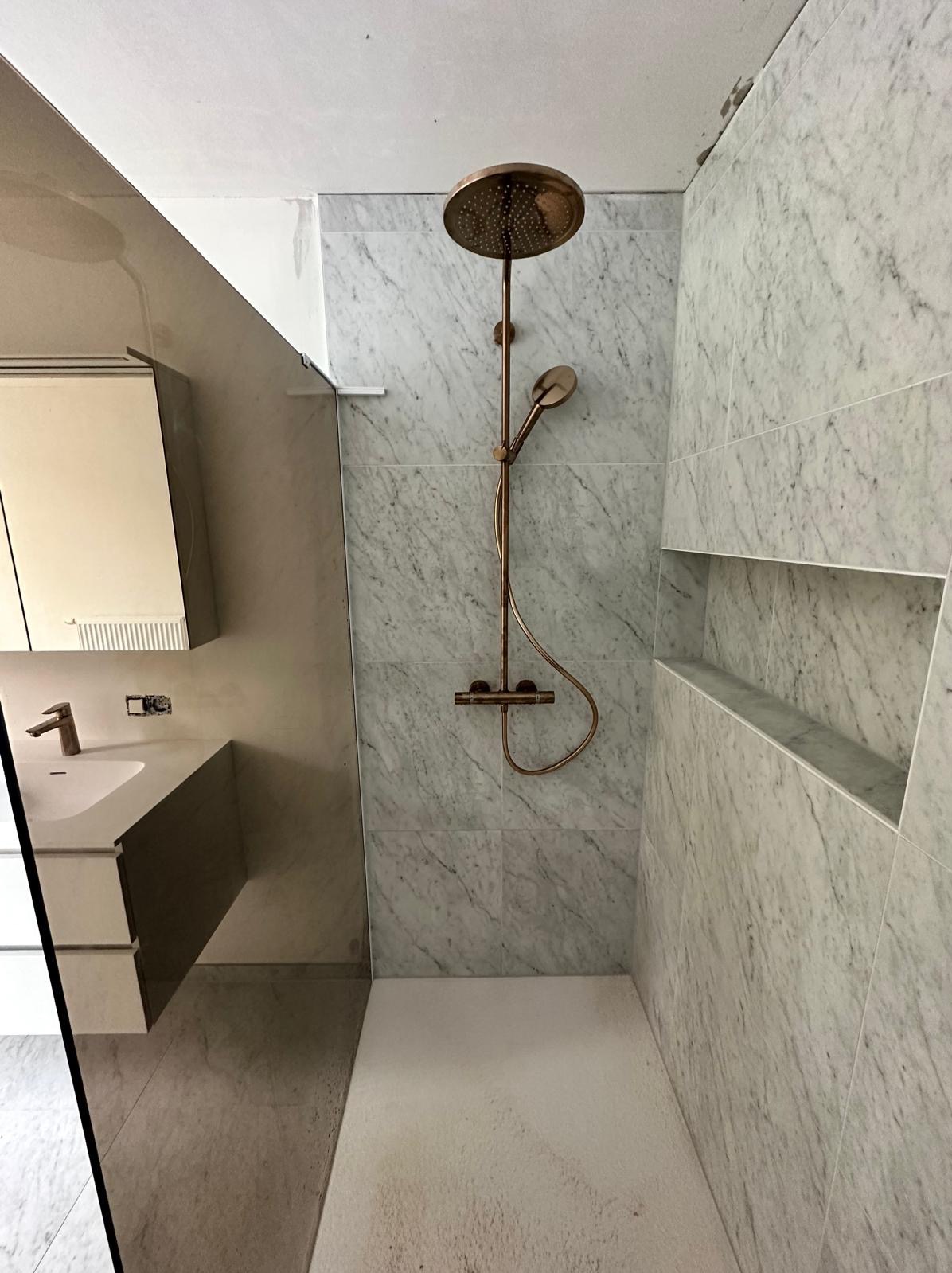 Nowoczesna łazienka w trakcie remontu: marmurowe płytki, miedziana armatura prysznicowa, wnęka w ścianie i minimalistyczna umywalka z szafką.