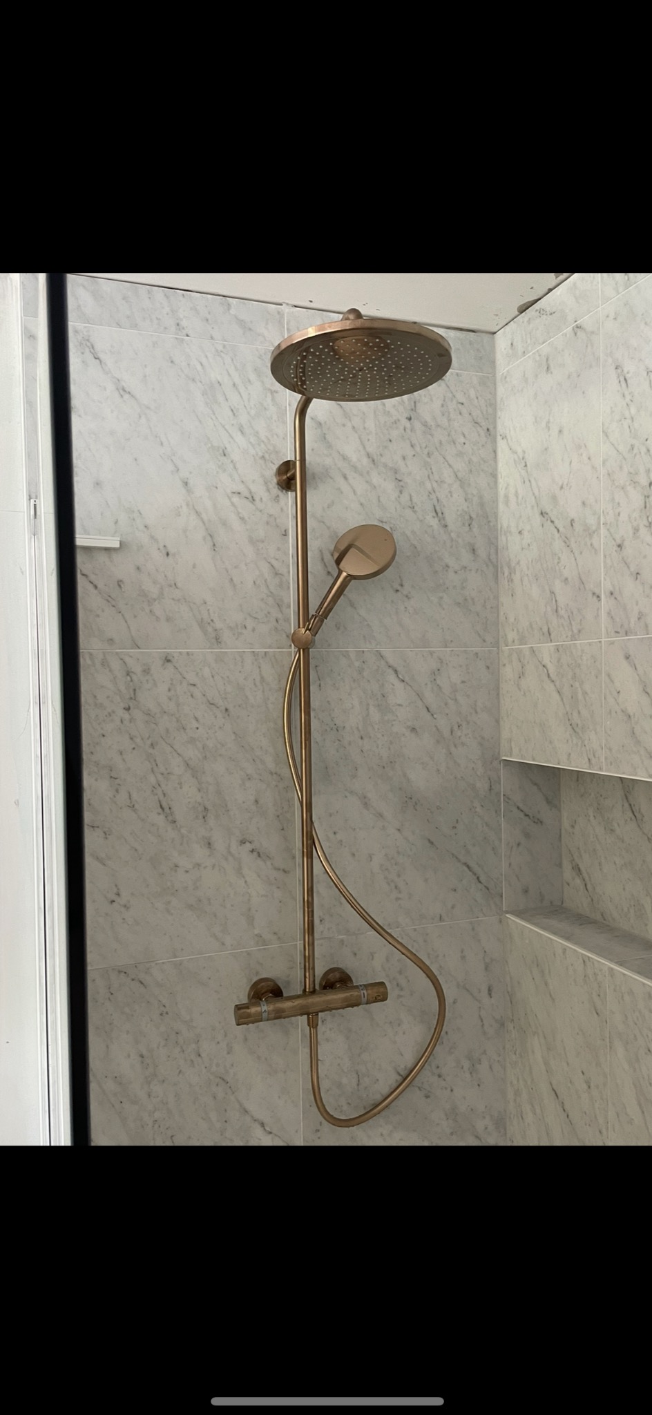 Miedziana bateria prysznicowa z deszczownicą i słuchawką, zamontowana na ścianie z marmurowych płytek w wykończonej łazience.