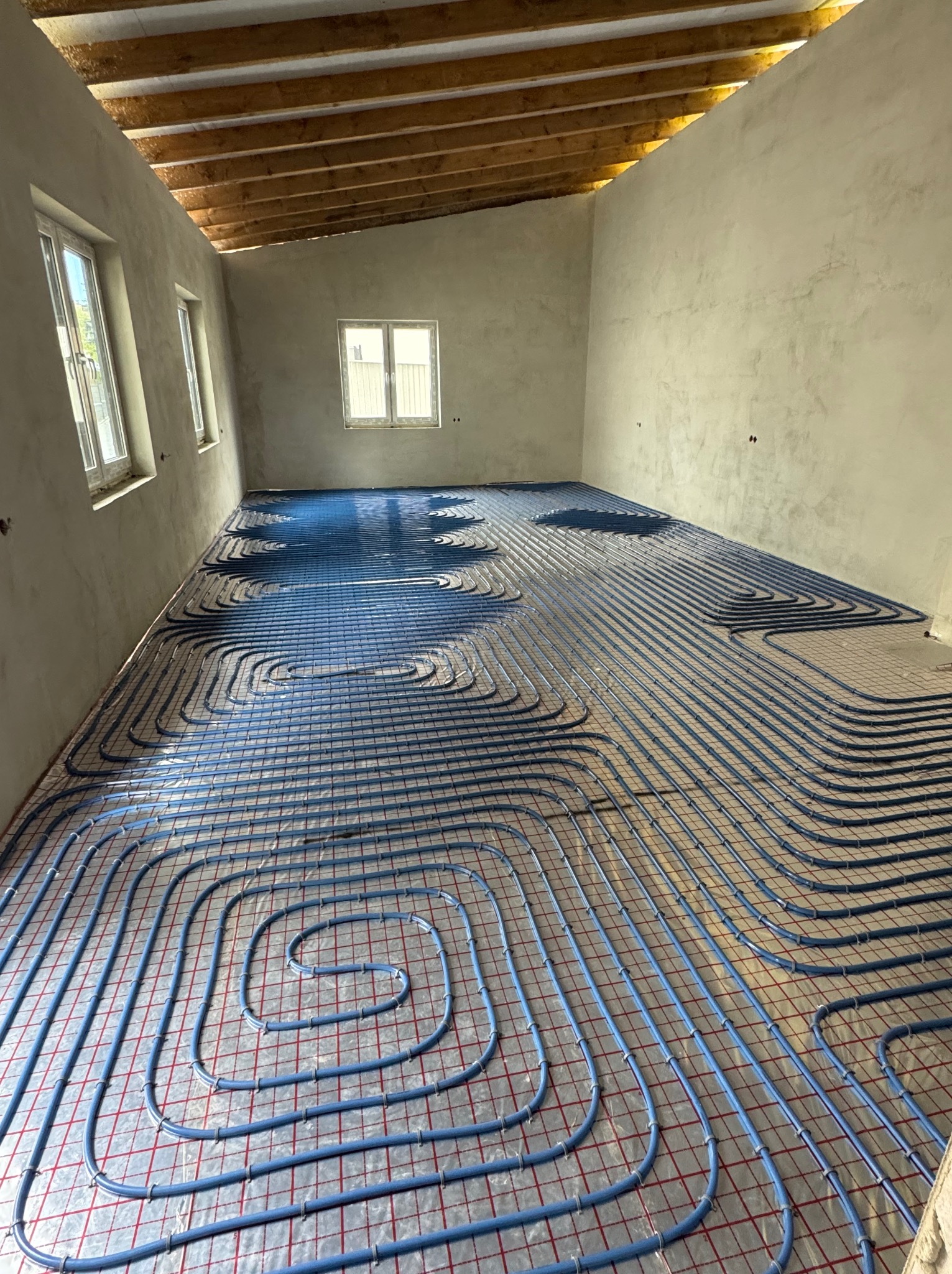 Niebieskie rury ogrzewania podłogowego na folii z siatką w surowym wnętrzu. Montaż instalacji w Cieszanowie przed wylaniem posadzki.