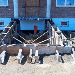 C&W Building sp. z o.o. - Szczegółowe ujęcie deskowania fundamentów domu z cegły, z widoczną izolacją termiczną i zbrojeniem, w trakcie budowy. Ujęcie z poziomu gruntu.