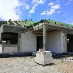 C&W Building sp. z o.o. - Stan surowy otwarty domu jednorodzinnego w Gogołowej. Widoczne ściany z betonu komórkowego, więźba dachowa zaimpregnowana na zielono i paleta z bloczkami.