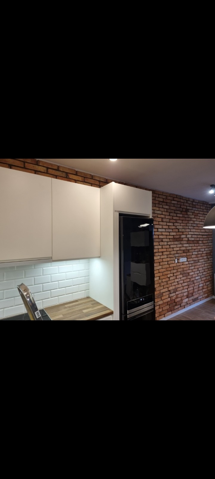 Nowoczesna kuchnia z białymi szafkami, ceglaną ścianą i białymi płytkami metra na ścianie nad blatem.