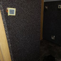 Usługi Remontowo-Budowlane WIETRZYŃSKI - Ściana w korytarzu pokryta ciemną, błyszczącą tapetą strukturalną. Widoczne gniazdka elektryczne w trakcie montażu i fragment drewnianej futryny drzwiowej.