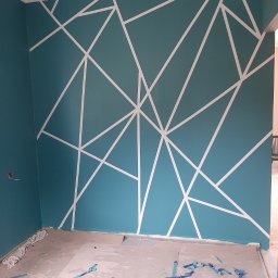 Usługi Remontowo-Budowlane WIETRZYŃSKI - Turkusowa ściana z białymi, geometrycznymi wzorami, świeżo po malowaniu. Na podłodze leżą resztki taśmy malarskiej. Widok na róg pokoju.