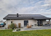 Dom jednorodzinny z panelami słonecznymi na dachu, widoczne z poziomu trawnika, pochmurne niebo w tle.