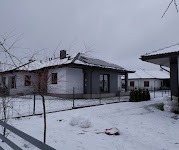 Dom jednorodzinny z panelami słonecznymi na dachu, pokryty śniegiem w zimowy dzień, widoczny zza ogrodzenia.