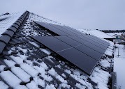 Panele słoneczne na dachu pokrytym śniegiem, widok z góry, pochmurne zimowe niebo w tle.