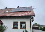 Panele słoneczne na czerwonym dachu domu jednorodzinnego w pochmurny dzień, widoczne okna i antena.