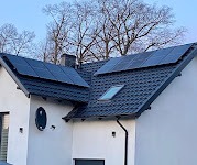 Panele słoneczne na dachu domu jednorodzinnego w Bielsku-Białej, widoczne z poziomu gruntu, z anteną satelitarną na ścianie.