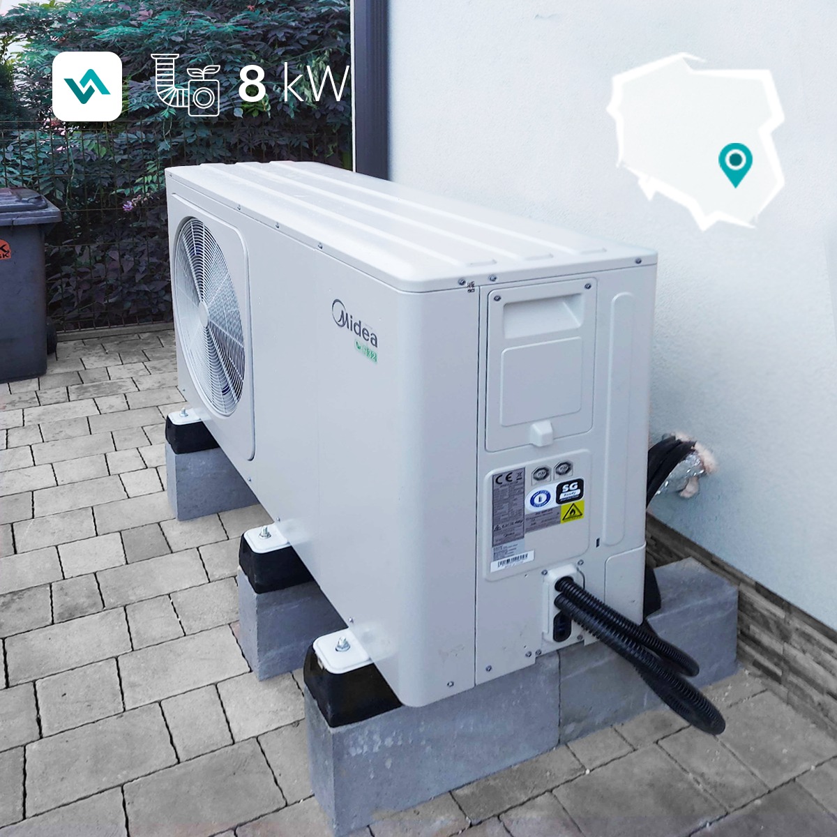 Biała zewnętrzna jednostka pompy ciepła Midea, zamontowana na betonowych bloczkach z gumowymi podkładkami, widoczne czarne rury przyłączeniowe, tło to kostka brukowa i zielona roślinność.