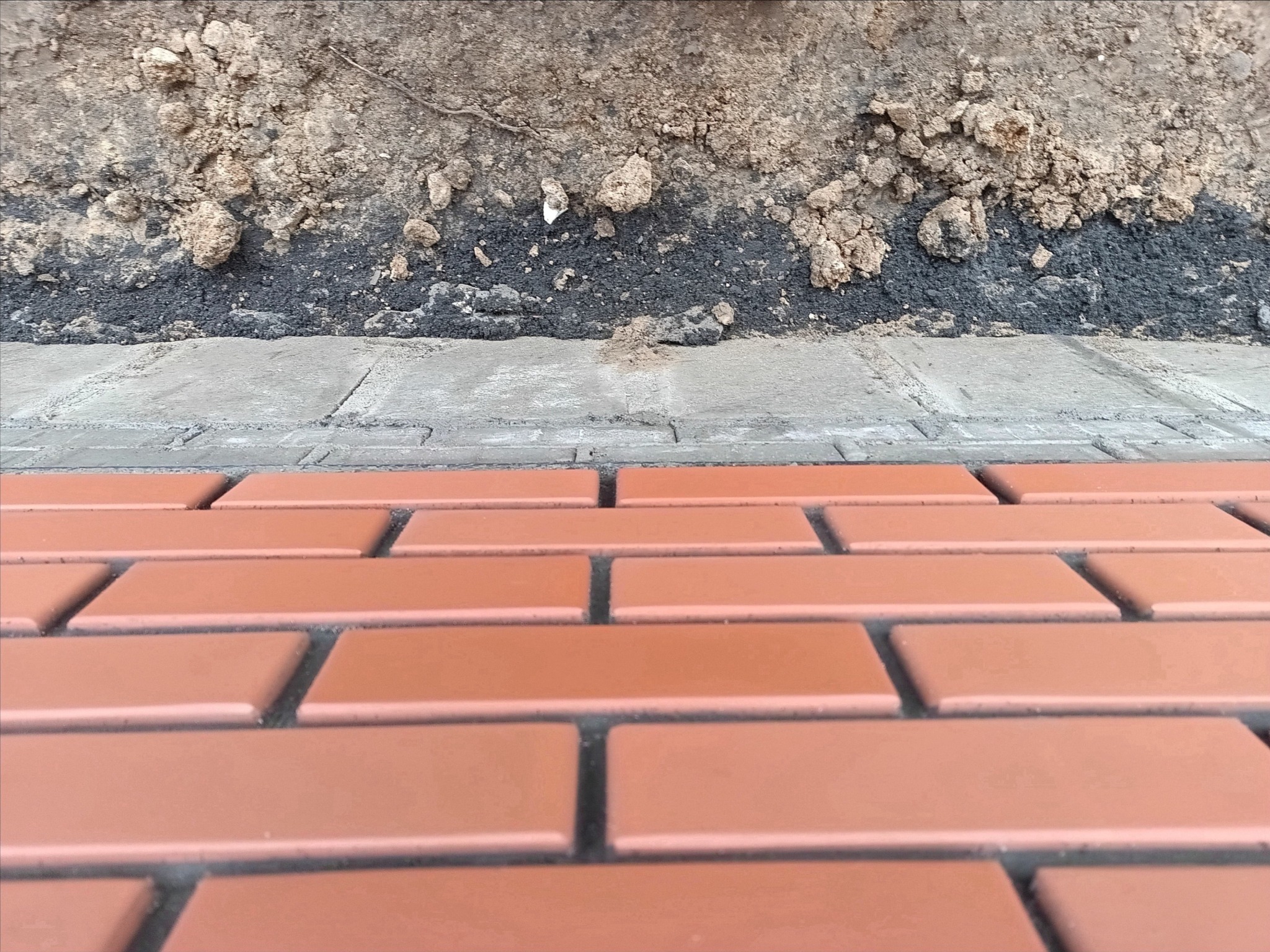 Ułożona, nowa, czerwona kostka brukowa na podsypce z ziemi i piasku, widok z niskiej perspektywy, ukazujący detale fug i fakturę materiałów.