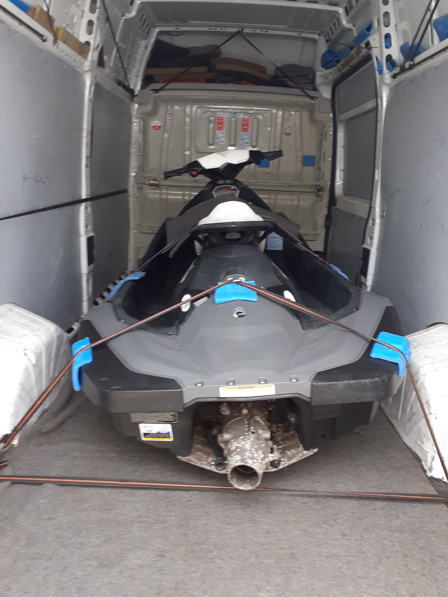 Szary skuter wodny zabezpieczony pasami wewnątrz furgonetki z otwartymi drzwiami, widoczny silnik i dysza.