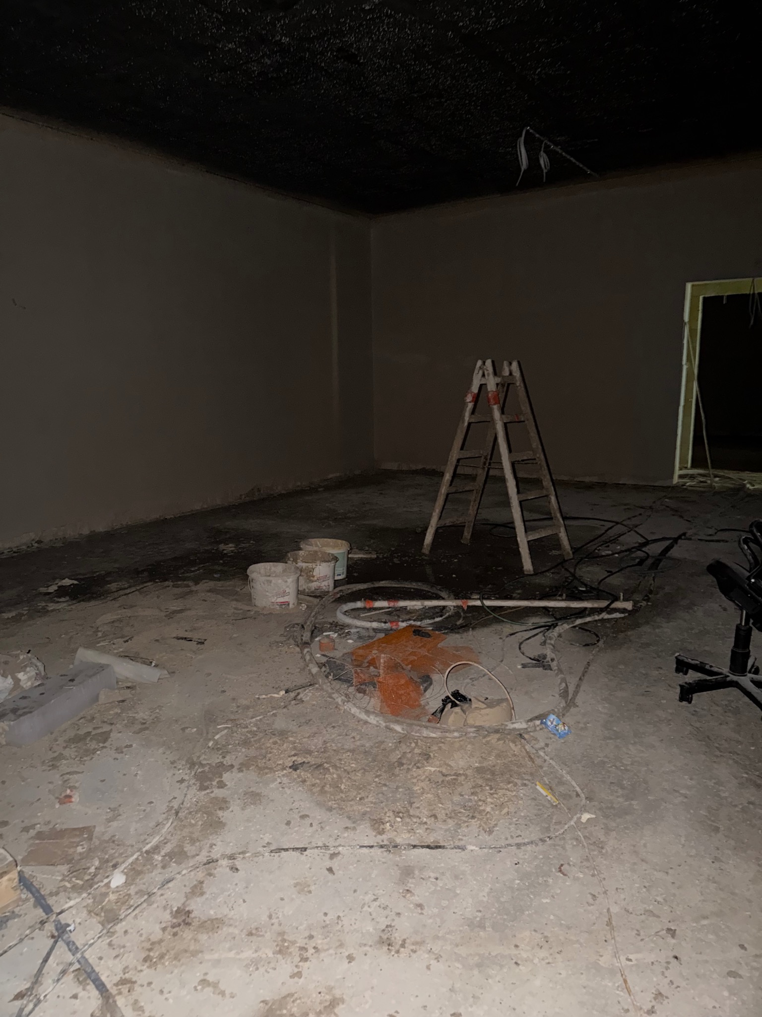 Wnętrze po tynkowaniu: gładkie, szare ściany, drabina, wiaderka po farbie i przewody na podłodze. Widoczne ślady prac wykończeniowych.