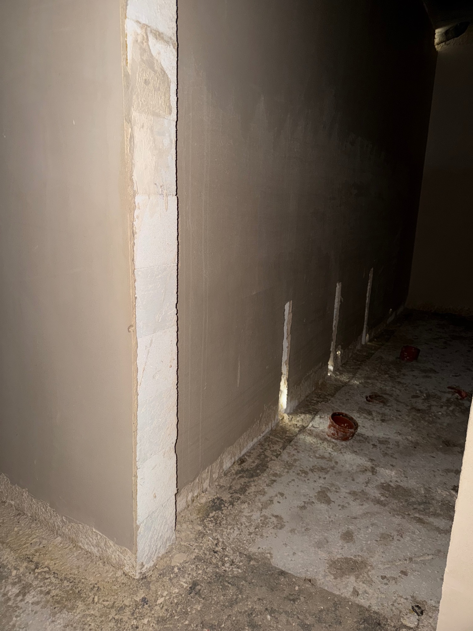 Świeżo nałożony tynk maszynowy na ścianie z widocznymi bruzdami pod instalacje. Szary odcień tynku kontrastuje z surowym betonem podłoża.