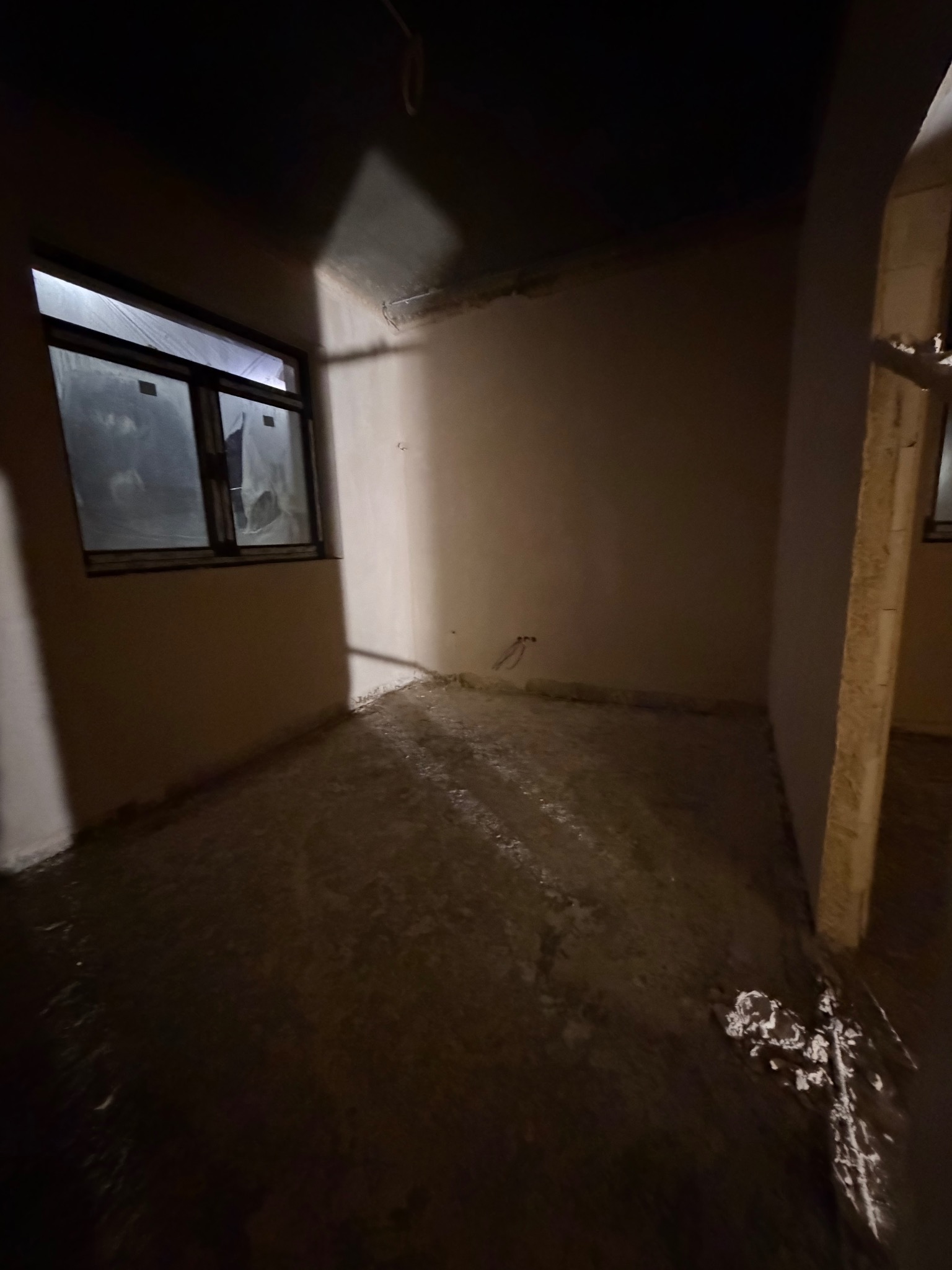 Pokój po nałożeniu tynków: gładkie ściany, widoczne okno z folią ochronną, surowa podłoga. Przygotowanie do dalszych prac wykończeniowych w nowym budownictwie.