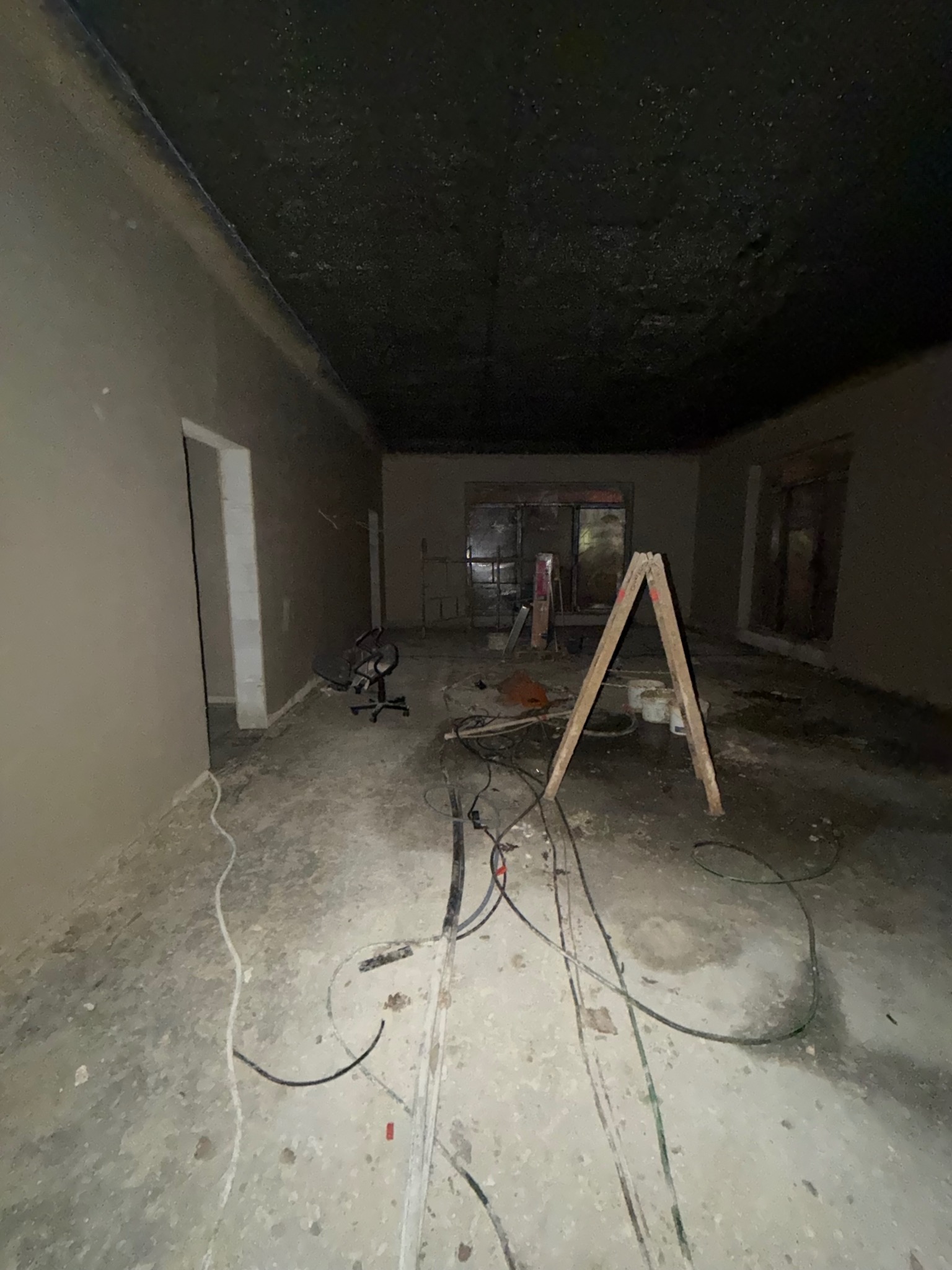Wnętrze po tynkowaniu ścian i sufitu. Widoczne kable na podłodze, drabina malarska i krzesło biurowe. Świeżo położony tynk ma jasnoszarą barwę.