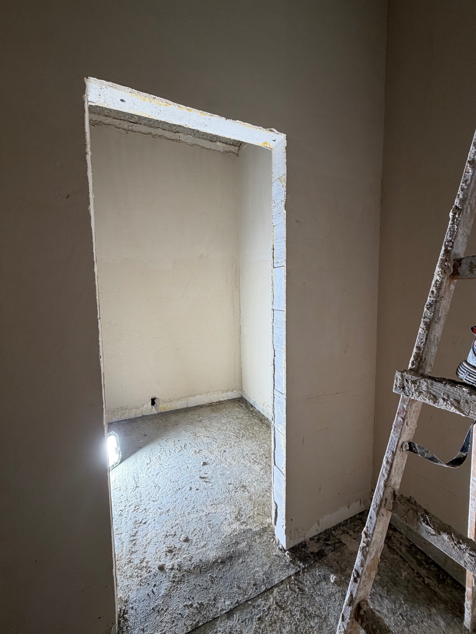 Wnętrze po tynkowaniu maszynowym: gładkie ściany, surowy otwór drzwiowy i drabina malarska. Widoczne ślady zaprawy na podłodze. Oświetlenie punktowe.