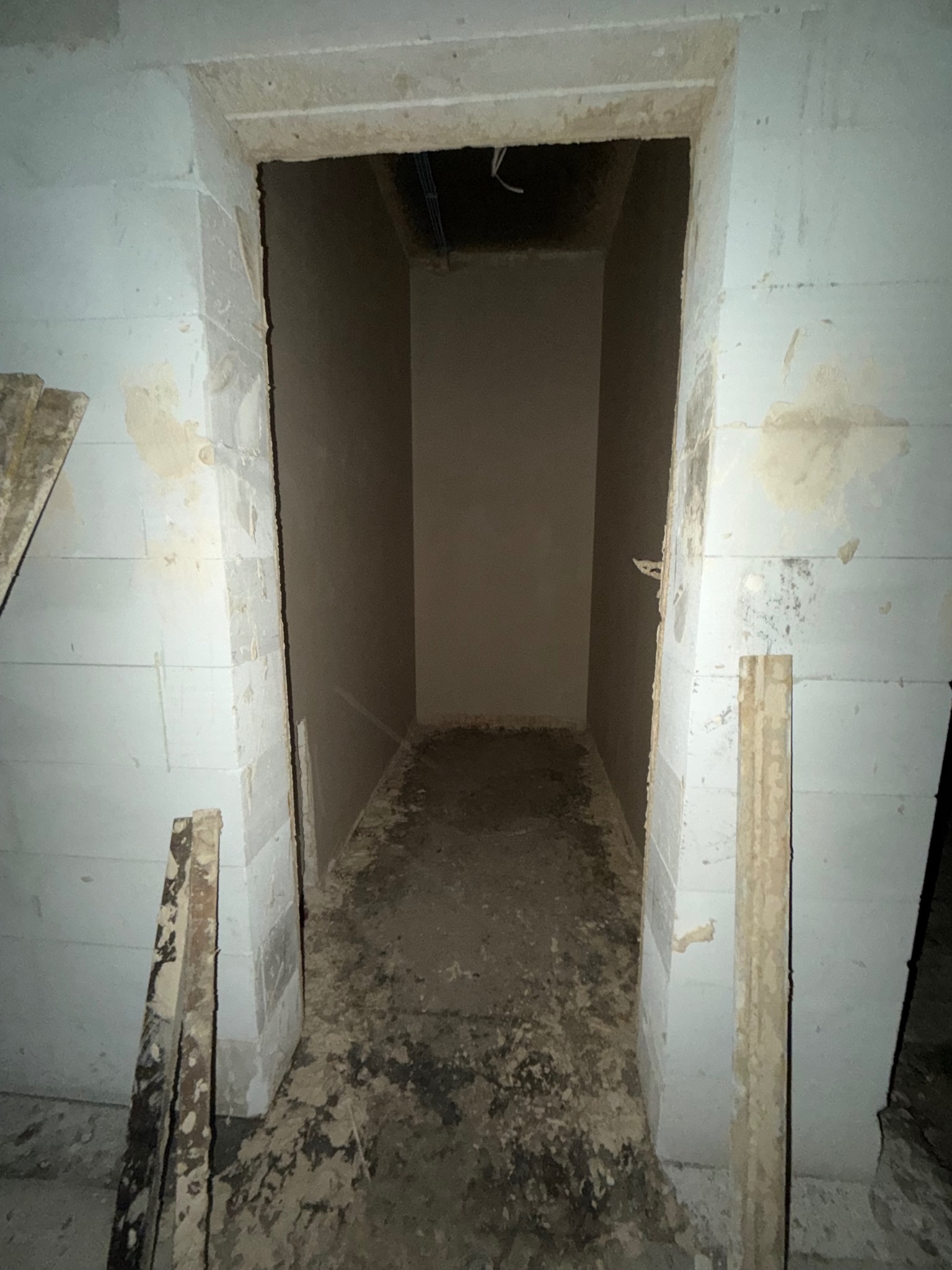 Wnętrze piwnicy po tynkowaniu maszynowym. Widoczne ślady zaprawy na podłodze i świeżo otynkowane ściany z bloczków. Surowe wykończenie, przygotowane do dalszych prac.